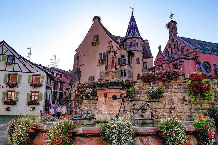 Blumengeschmückte Häuser und Brunnen an der Place du Château Saint-Léon in Eguisheim.
